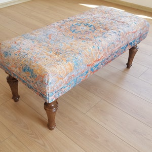 Peut inclure: Un ottoman à motifs avec un design de tapis coloré. L'ottoman a quatre pieds en bois.