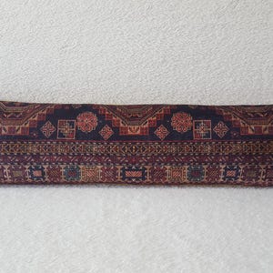 Peut inclure: Un long coussin rectangulaire avec un fond bleu foncé et un motif géométrique coloré dans les tons de rouge, orange et jaune. Le coussin est fait d'un tissu doux et tissé.