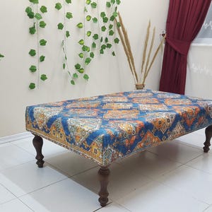 Peut inclure: Un ottoman bleu et orange &agrave; motifs avec des pieds en bois. L'ottoman est pos&eacute; sur un sol en carrelage blanc.