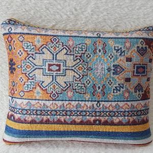 May include: A decorative cushion with a blue, orange and yellow geometric pattern. The cushion has a woven texture and a fringed edge.
