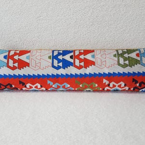 May include: A long, rectangular pillow with a colorful geometric pattern. The pillow is made of a white fabric with red, blue, green, and black geometric shapes. The pillow is perfect for adding a touch of color and style to any room.