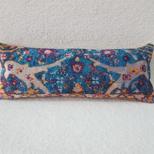 Könnte beinhalten: Ein langes, rechteckiges Kissen mit einem blauen, orangefarbenen und weißen gemusterten Stoff. Das Muster zeigt komplizierte florale Designs und geometrische Formen.