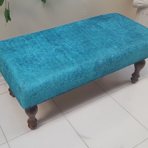 May include: A teal blue upholstered bench with wooden legs. The bench is sitting on a white tiled floor.