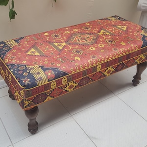 Peut inclure: Un ottoman rouge, jaune et bleu à motifs avec des pieds en bois. L'ottoman est recouvert d'un tissu à motifs traditionnels.