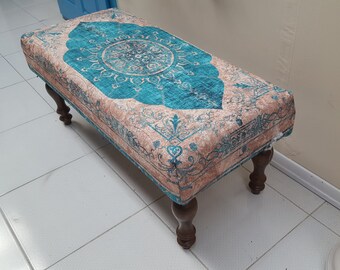 May include: A teal and beige patterned ottoman with wooden legs. The ottoman has a traditional design with a central medallion and floral motifs.