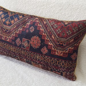 May include: A rectangular cushion with a dark blue background and a colourful geometric pattern in shades of red, orange, and gold. The pattern features intricate designs and motifs.
