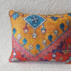 May include: A decorative throw pillow featuring a colourful geometric pattern in shades of red, orange, blue, and white. The pillow has a yellow background and a traditional rug-like design.