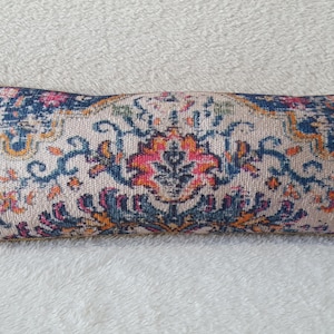 May include: A long rectangular pillow with a cream background and a colorful floral pattern. The pattern features blue, pink, orange, and yellow colors.