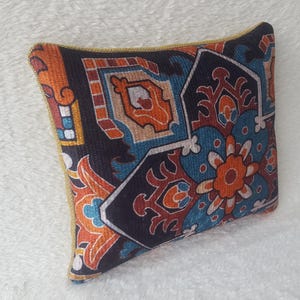 May include: A decorative cushion with a geometric pattern in shades of blue, orange, and red on a black background. The cushion has a gold trim.