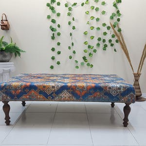 Peut inclure: Un ottoman bleu et orange &agrave; motifs avec des pieds en bois. L'ottoman est pos&eacute; sur un sol en carrelage blanc.