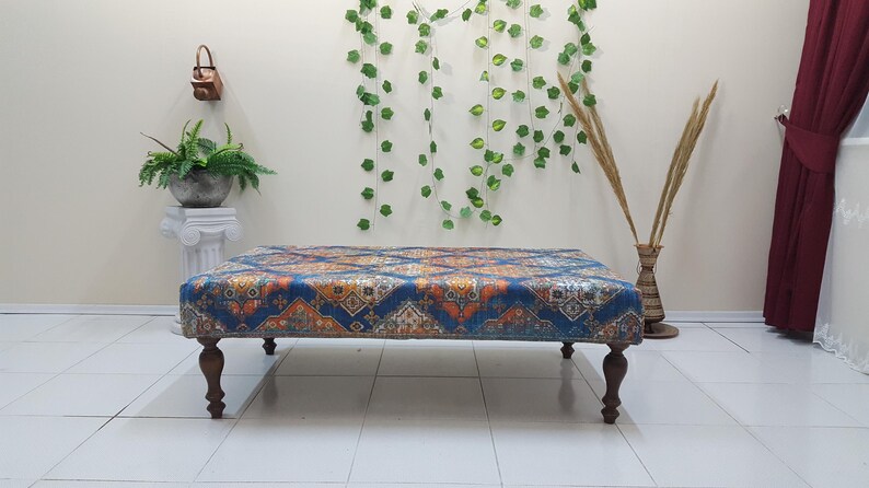 Peut inclure: Un ottoman bleu et orange &agrave; motifs avec des pieds en bois. L'ottoman est pos&eacute; sur un sol en carrelage blanc.