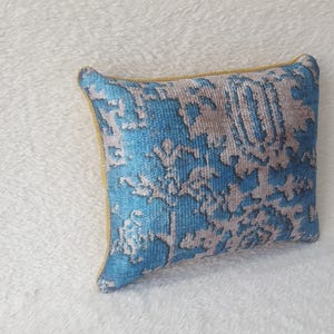 May include: A blue and white patterned cushion with a yellow border. The cushion is made of a soft, plush fabric.