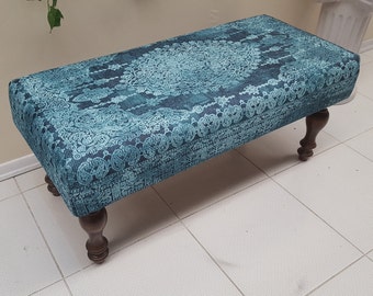 May include: A teal blue ottoman with a patterned fabric top and four dark brown wooden legs.
