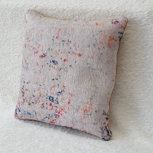 May include: A white cushion with a colourful abstract pattern. The cushion has a soft, textured fabric and is ideal for adding a touch of colour to any room.