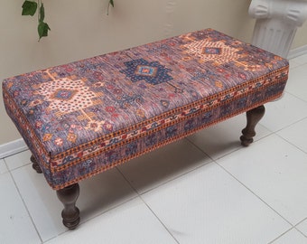 May include: A rectangular ottoman with a dark purple, orange, and blue patterned fabric top and dark brown wooden legs.