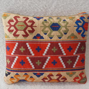 May include: A decorative cushion with a geometric pattern in shades of red, blue, green, and white. The cushion is made of a soft, textured fabric.