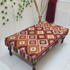 May include: A rectangular ottoman with a colorful geometric pattern woven into the fabric. The ottoman has four wooden legs.