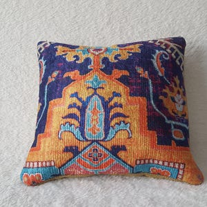Könnte beinhalten: Ein dekoratives Kissen mit einem farbenfrohen, komplizierten Muster in Orange, Blau und Gelb. Das Muster ähnelt einem traditionellen Teppich oder Wandteppich.