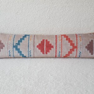 May include: A long, rectangular throw pillow with a beige background and a geometric pattern in shades of red, orange, blue, and brown.