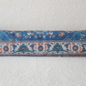 May include: A long, rectangular blue and white patterned throw pillow with a floral design. The pillow is made of fabric and has a soft, comfortable texture.