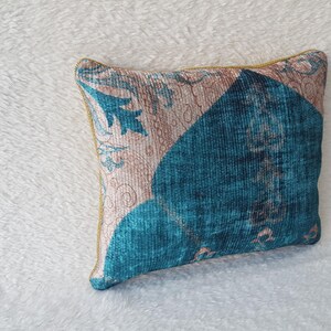 May include: A decorative cushion with a blue and pink floral pattern. The cushion has a gold trim and is made of a soft, textured fabric.