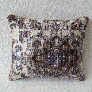 May include: A decorative cushion with a brown, cream and blue patterned design. The cushion is made of a soft, woven fabric and has a square shape.