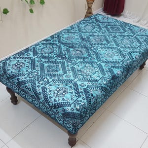 May include: A blue and black patterned ottoman with wooden legs. The ottoman has a square top and a geometric design.