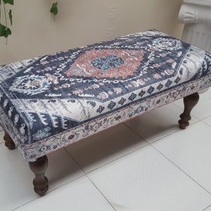 May include: A decorative ottoman with a patterned fabric top in shades of blue, white, and pink. The ottoman has four wooden legs.