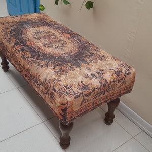 Peut inclure: Un banc en bois brun avec un coussin en tissu à motifs. Le coussin présente un motif floral dans des tons orange, brun et noir.