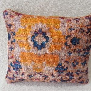 Könnte beinhalten: Ein quadratisches Kissen mit einem farbenfrohen Muster. Das Kissen zeigt ein Blumenmuster in Orange-, Blau- und Rosatönen.