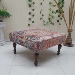 May include: A square ottoman with a colorful patterned fabric top and four wooden legs. The ottoman is sitting on a white tiled floor.