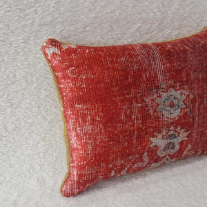 May include: Red and white patterned cushion with a gold trim. The cushion is made of a soft, textured fabric.