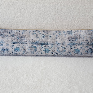 May include: A long, rectangular throw pillow with a white background and a blue and gray patterned design. The pillow is made of a soft, textured fabric.