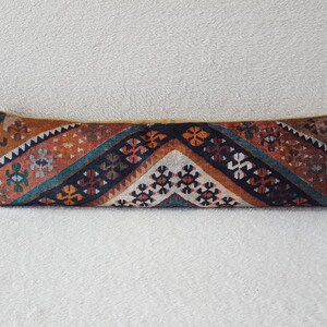 May include: A long, rectangular pillow with a colorful geometric pattern. The pillow is made of a woven fabric with a variety of colors, including red, orange, blue, and black. The pattern is intricate and detailed, and the pillow is a great addition to any home.