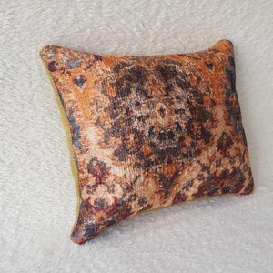 May include: A decorative throw pillow with a colourful, intricate pattern in shades of orange, brown, and purple. The pillow has a gold trim around the edges.