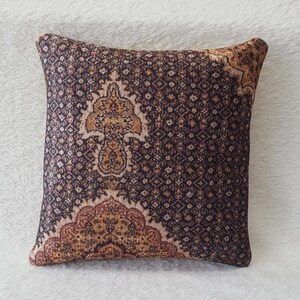 May include: A decorative cushion with a brown and beige paisley pattern. The cushion has a dark brown background with a repeating pattern of small diamonds and a larger paisley design in the centre.
