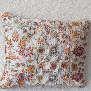May include: A white cushion with a floral pattern in shades of orange, red, and blue. The cushion is made of a soft, textured fabric.