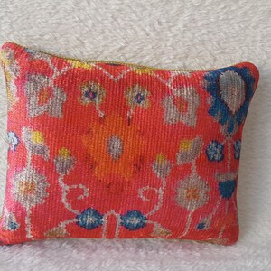 May include: A red, yellow, blue and white patterned throw pillow with a floral design.