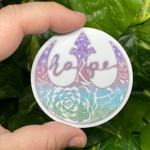 May include: A white sticker with a pink, blue, and green gradient. The sticker features a floral design with the word "hope" written in a cursive font.