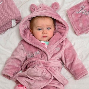 Babies personalised Dusky Pink hooded dressing gown. Made from super soft material, it features an elephant embroidery to the chest as well as detailing pom pom ears and a hood. Make it extra special by adding a personalised touch.