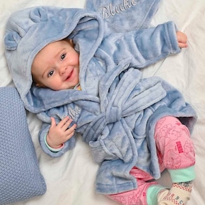 May include: A baby wearing a light blue hooded robe with the name "Blake" embroidered on it. The robe has a tie belt and is made of soft, plush fabric.