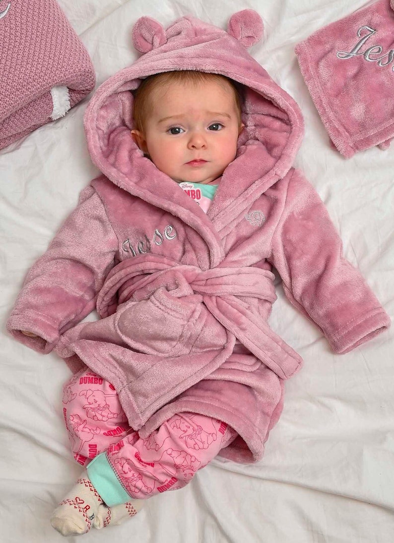 Babies personalised Dusky Pink hooded dressing gown. Made from super soft material, it features an elephant embroidery to the chest as well as detailing pom pom ears and a hood. Make it extra special by adding a personalised touch.