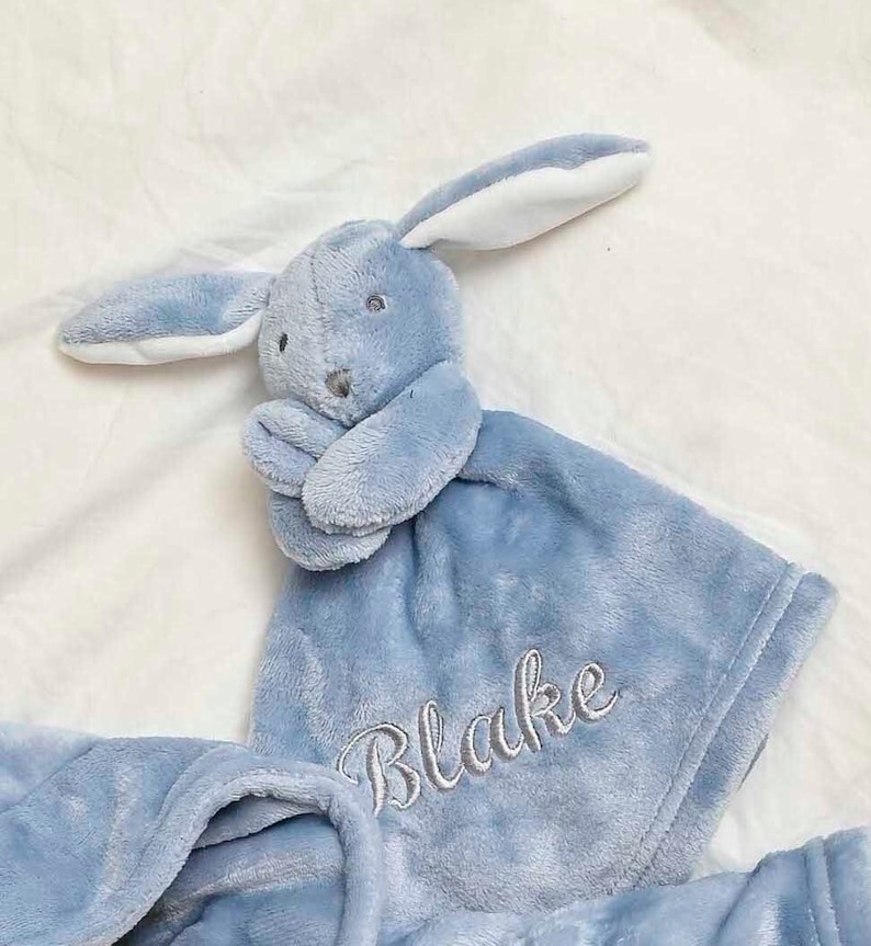 our Babies personalised bunny comforter in Dusky Blue is crafted from super soft plush material, this comforter will keep your baby snug and content. Complete with your babies name personalised/embroidered to the front.