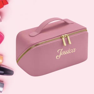 May include: A pink leather cosmetic bag with a gold zipper and handle. The bag has the name "Jessica" written in gold lettering.