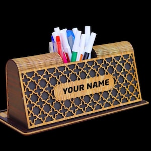 May include: A wooden desk organizer with a geometric pattern and a personalized nameplate that says "YOUR NAME". The organizer has a slot for pens and pencils and is made of light brown wood.