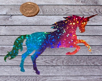 May include: A colorful unicorn silhouette with a glittery, rainbow gradient design. The unicorn is posed mid-stride, with a long horn and flowing mane. A gold coin is next to the unicorn. The background is a wooden surface.