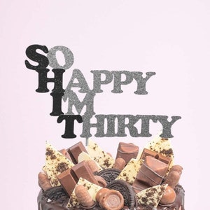 May include: A chocolate cake with a chocolate ganache drip and topped with chocolate candies, cookies, and a cake topper that reads "So Happy I'm Thirty".