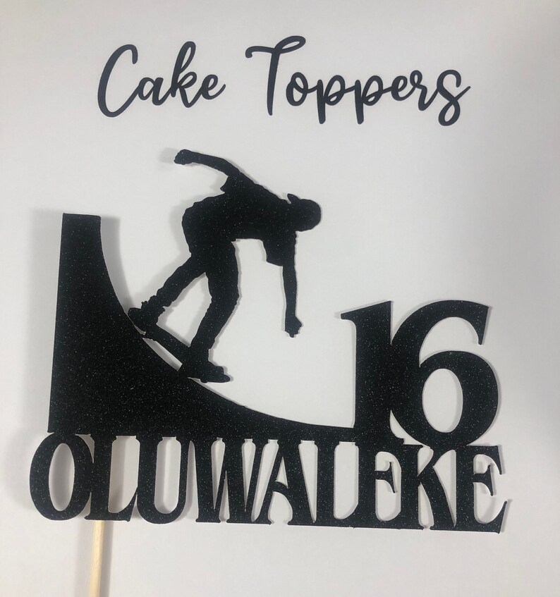May include: Black glitter cake topper featuring a silhouette of a skateboarder performing a trick on a half-pipe, the number 16, and the name Oluwaleake.