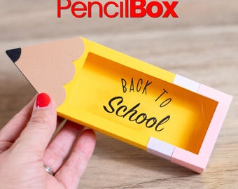 Op de afbeelding: Een gele papieren doos in de vorm van een potlood met een beige punt, een zwarte stift en een roze gum-uiteinde. De binnenkant bevat de zwarte tekst "BACK TO SCHOOL" in een cursief lettertype. Bovenaan staat de rode tekst "PencilBox".