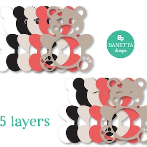 May include: Five layered die cut template of a teddy bear with a heart on its chest. The layers are white, black, beige, and pink.